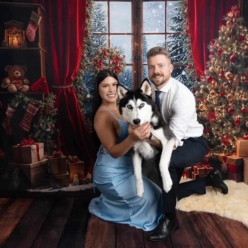 Paar sitzt mit einem Husky vor einer festlich dekorierten Weihnachtskulisse.
