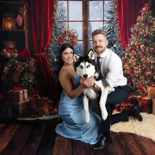 Paar posiert mit einem Husky vor einer festlich geschmückten Weihnachtskulisse.