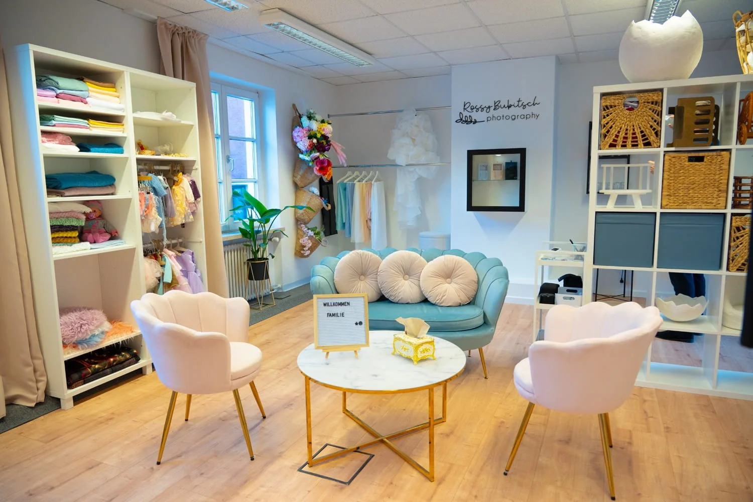Gemütliche Wartezone mit pastellfarbenem Sofa, weißen Sessel, runden Kissen, kleiner Marmortisch mit Willkommensschild.