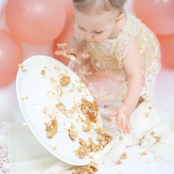 Kleines Kind bei einem Kindergeburtstag, das die Torte auf einem Teller umgestoßen hat, mit Krümeln und Zuckerguss