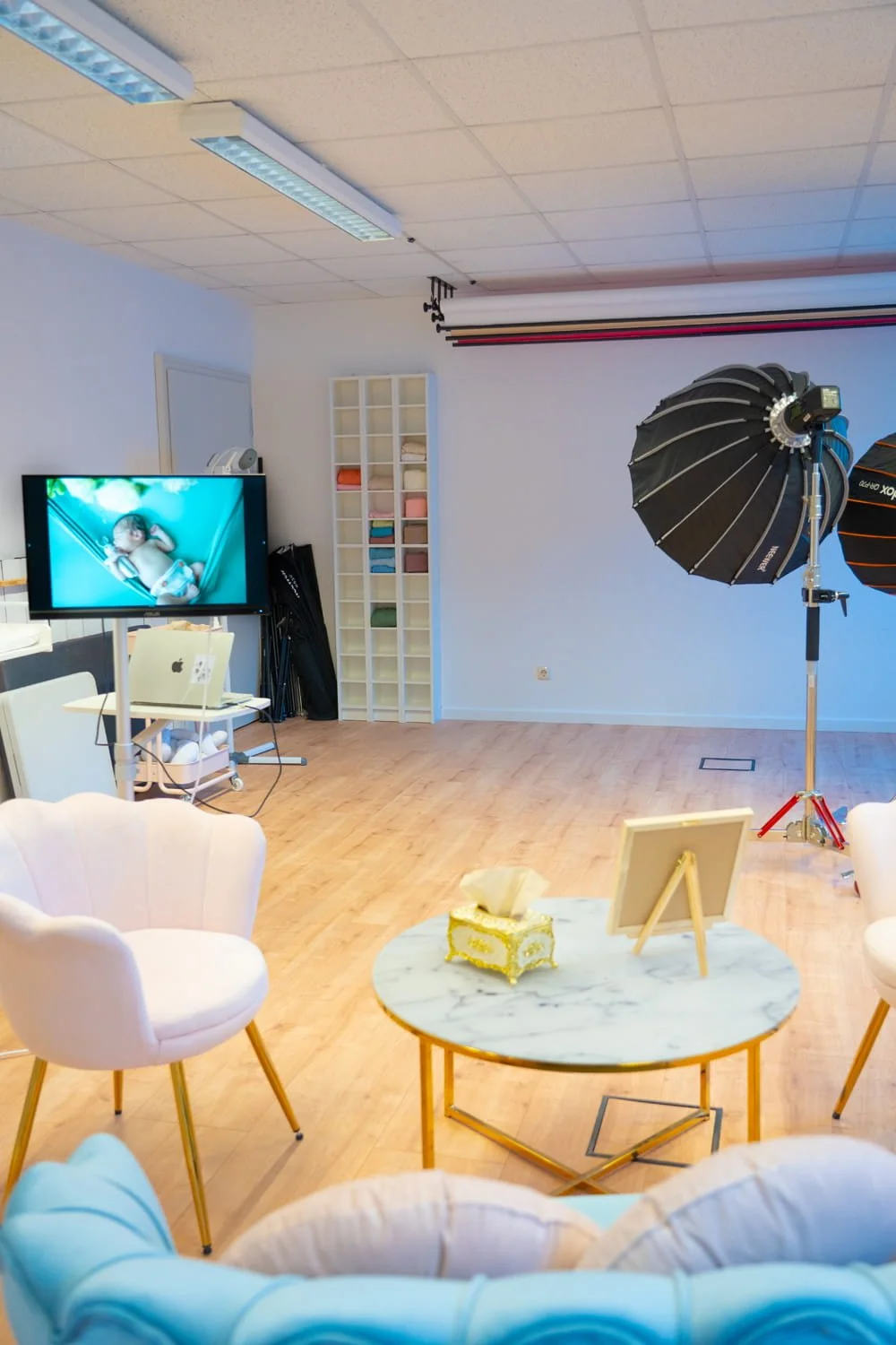 Fotostudio mit Fotobeleuchtung, Leinwand, Stühlen, einem Fernsehen mit einem Babyfoto.
