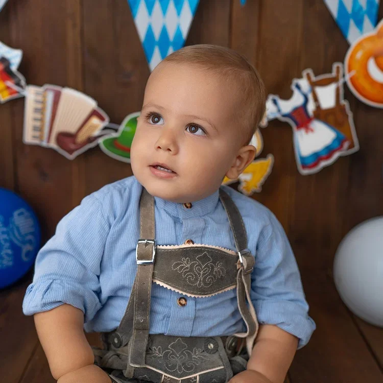 Kleiner Junge in bayerischer Tracht sitzt vor einer dekorierten Kulisse.