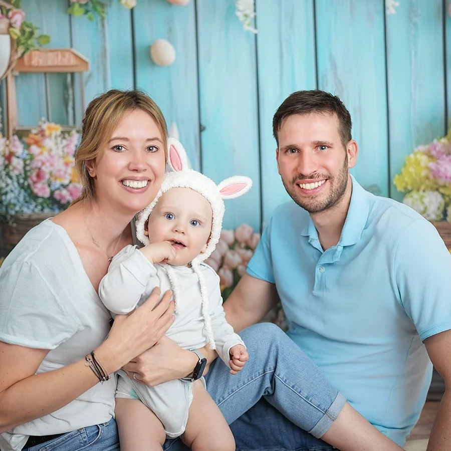 Familie mit einer jungen Frau, einem Mann, und einem Baby in einem blumigen Hintergrund.