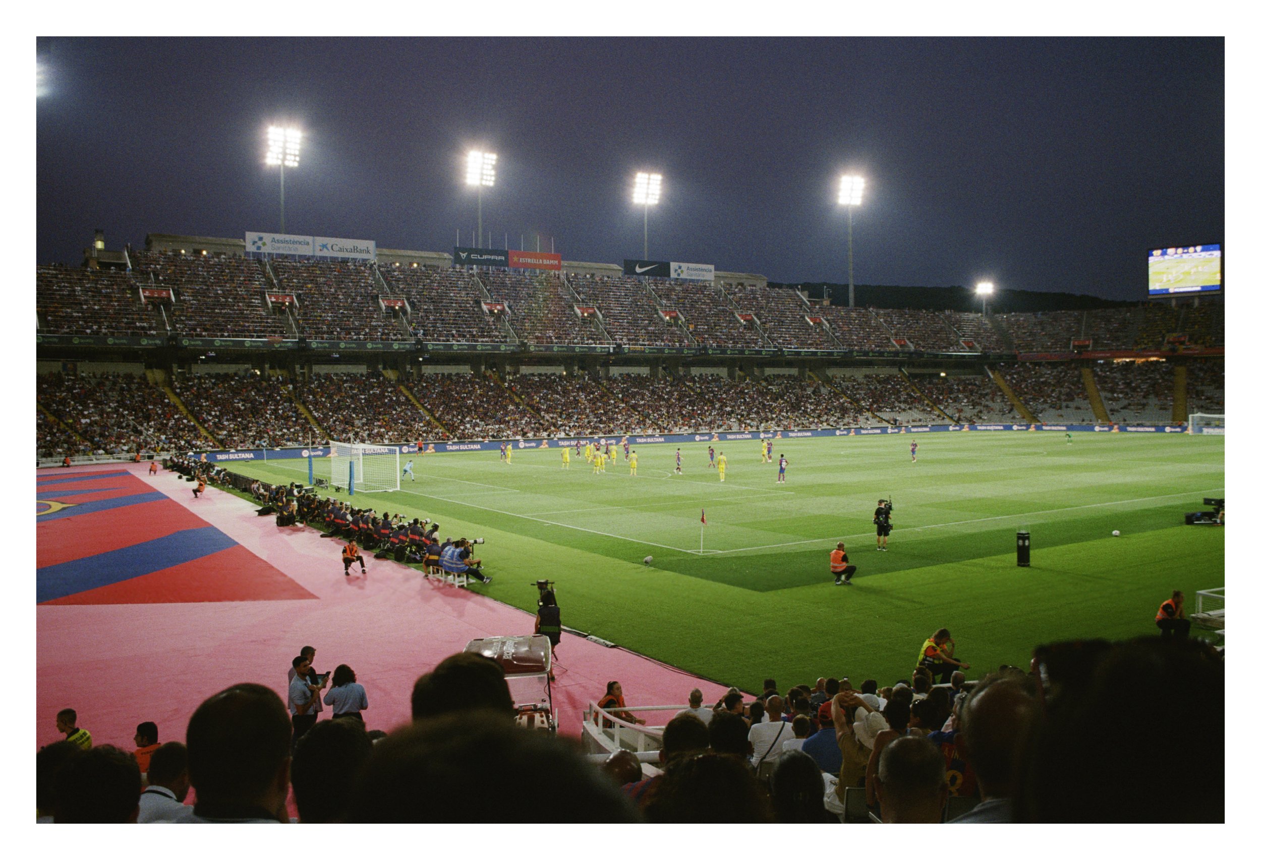 Soccer match at a stadium under floodlights with a packed crowd.