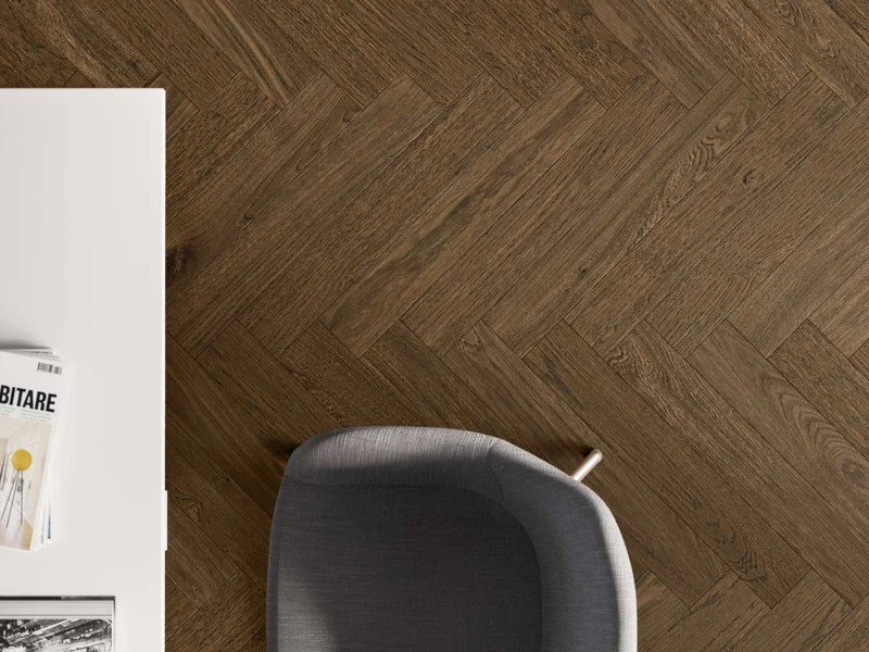 Parte di una scrivania bianca con riviste e fotografie, una sedia grigia e un pavimento in legno.