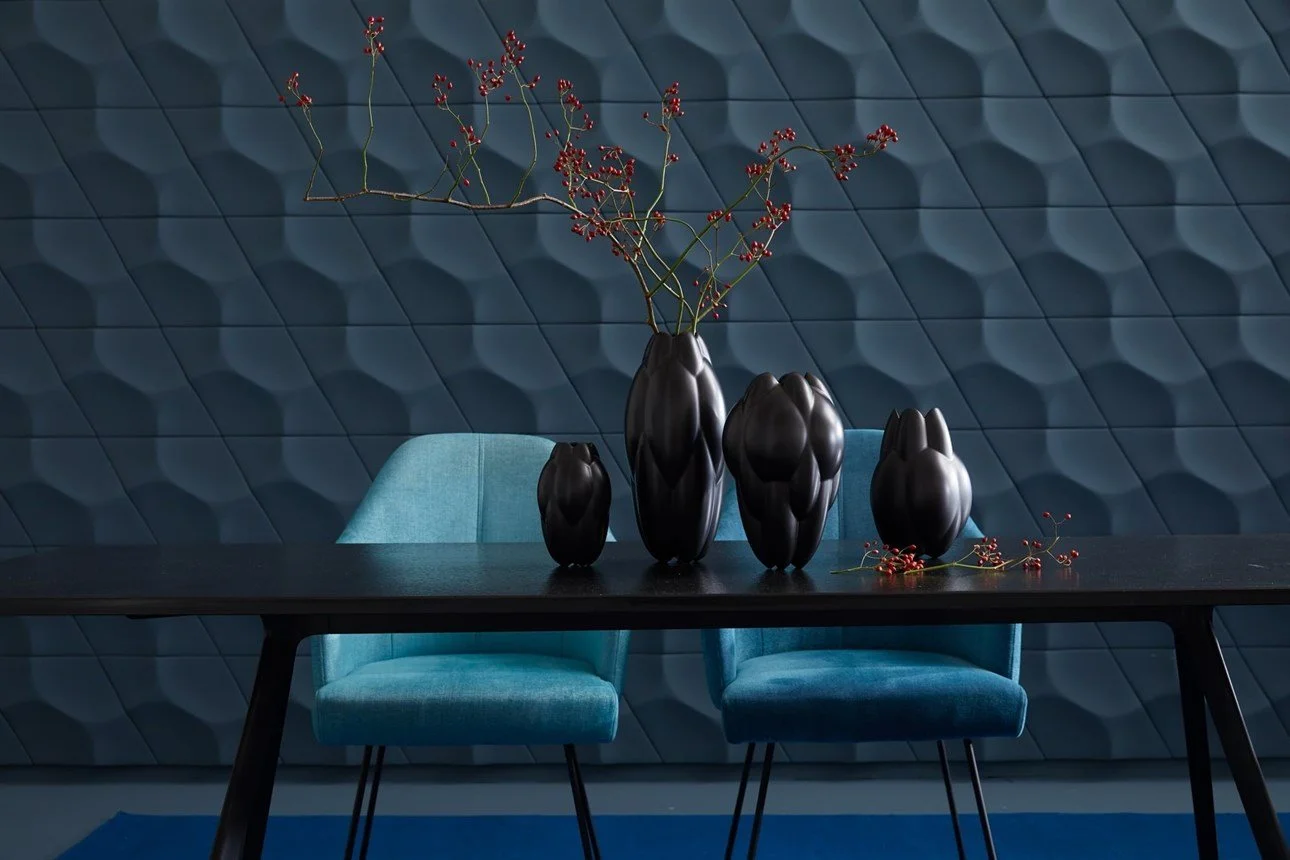 Vasi neri di forme diverse con rami con bacche rosse su un tavolo nero, sfondo con parete blu tripla