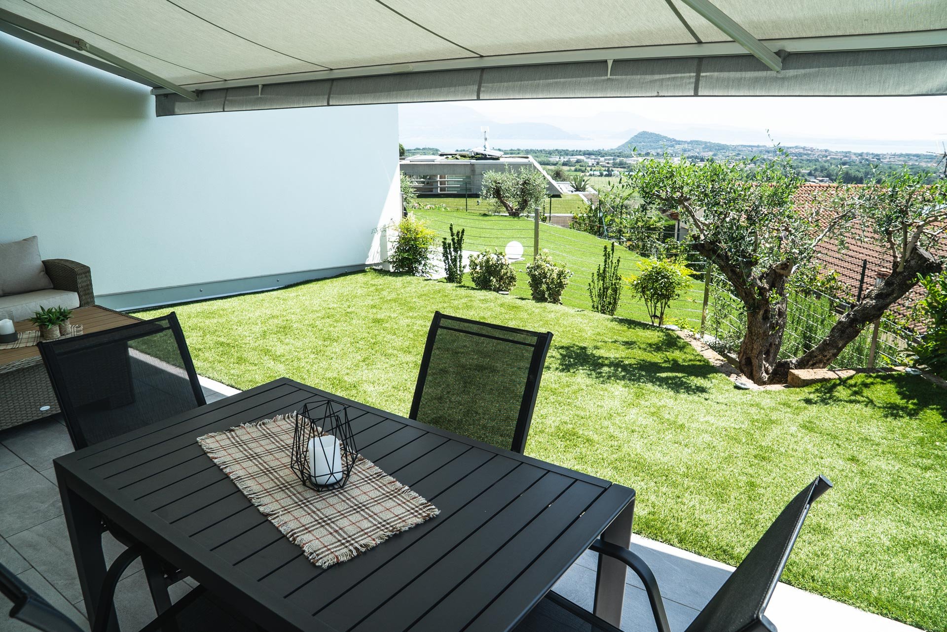 Veranda con tavolo e sedie, vista su giardino con alberi e paesaggio urbano e colline sullo sfondo.
