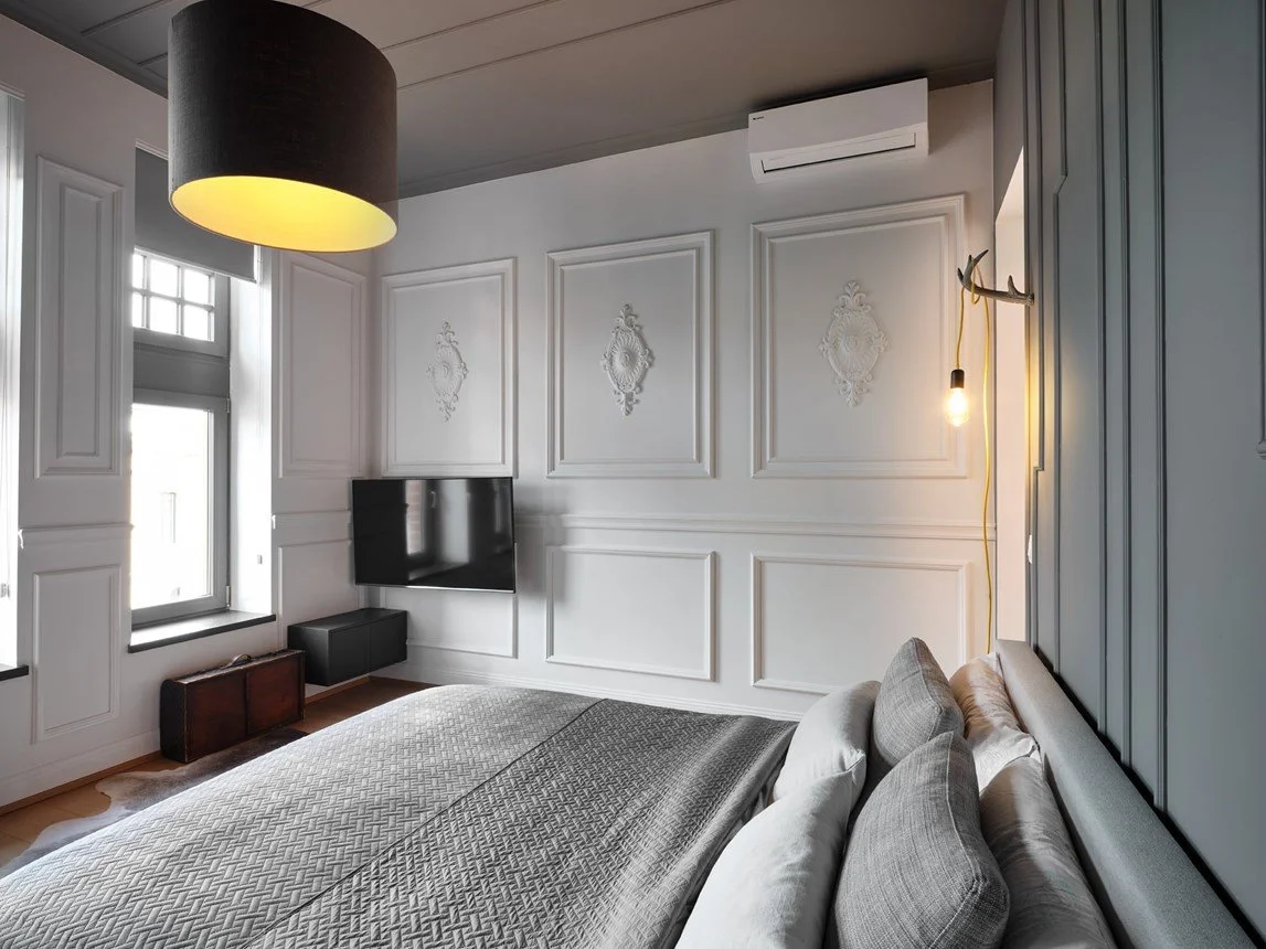 Camera da letto moderna con pareti decorate, grande letto con cuscini, televisore, lampada a soffitto e luce accecante, aria condizionata.