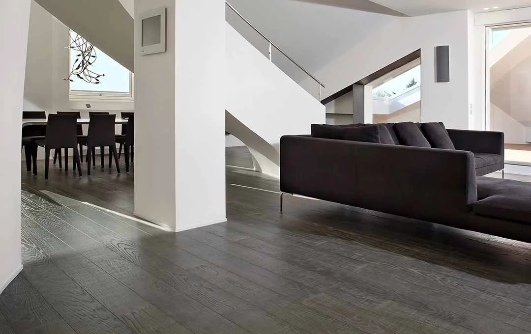 Interno di un soggiorno moderno con pavimento in legno, divano nero e scala bianca con parapetto in vetro.