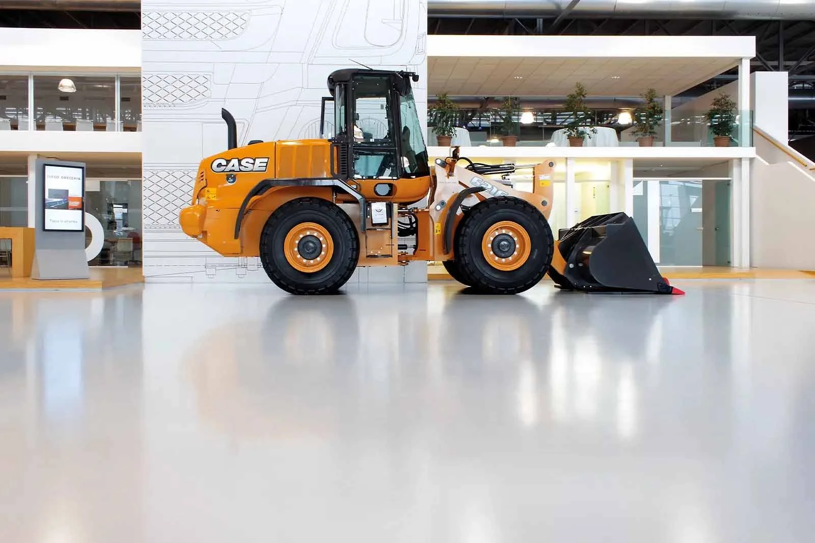 Escavatore giallo in un edificio moderno con pianta sulle scale interne e pannelli informativi.