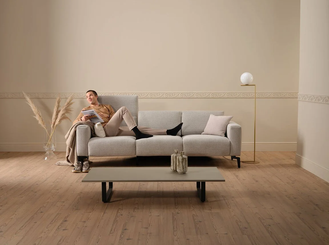 Persona che si riposa su un divano moderno in un soggiorno minimalista con decorazioni semplici, illuminata da una lampada a stelo dorata.