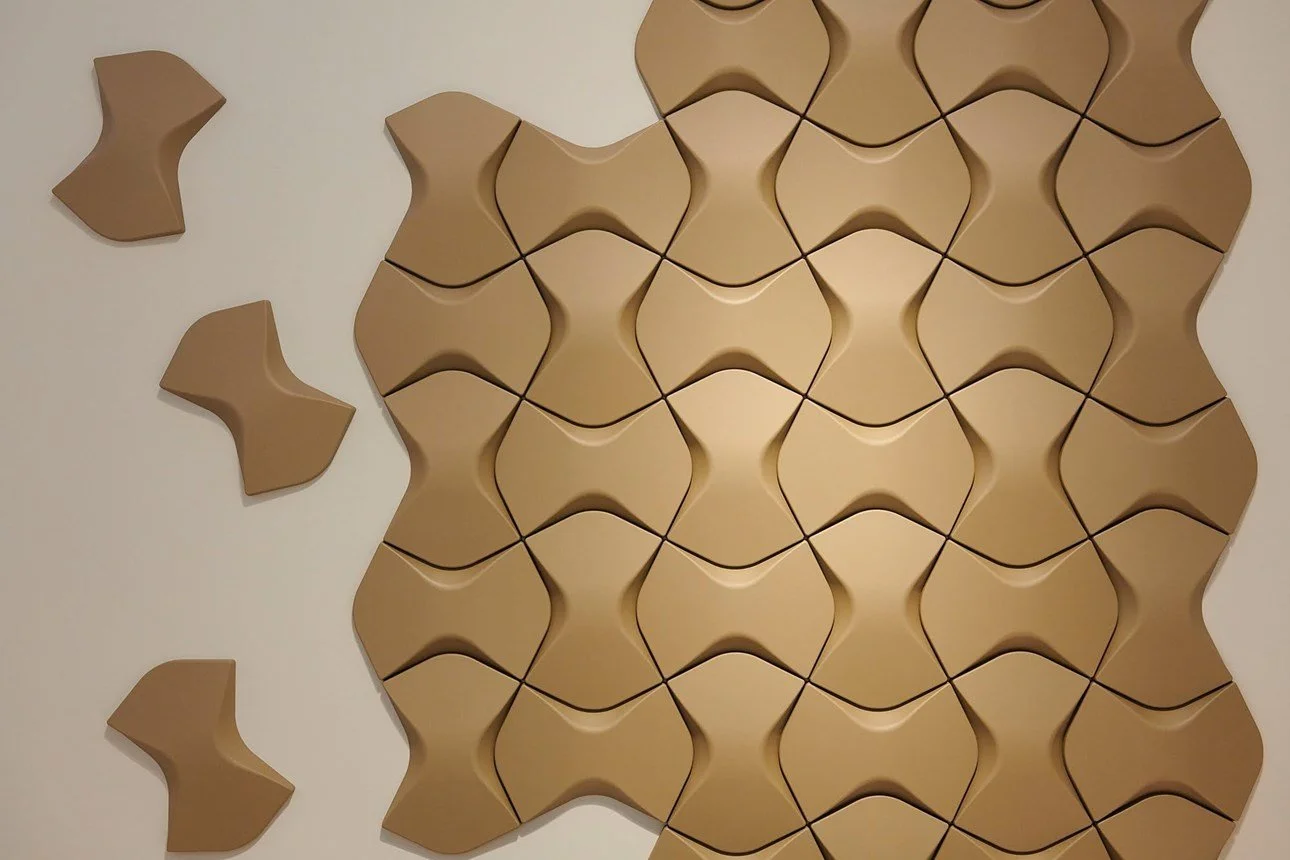 Pannelli acustici triangolari di colore beige applicati a una parete bianca.