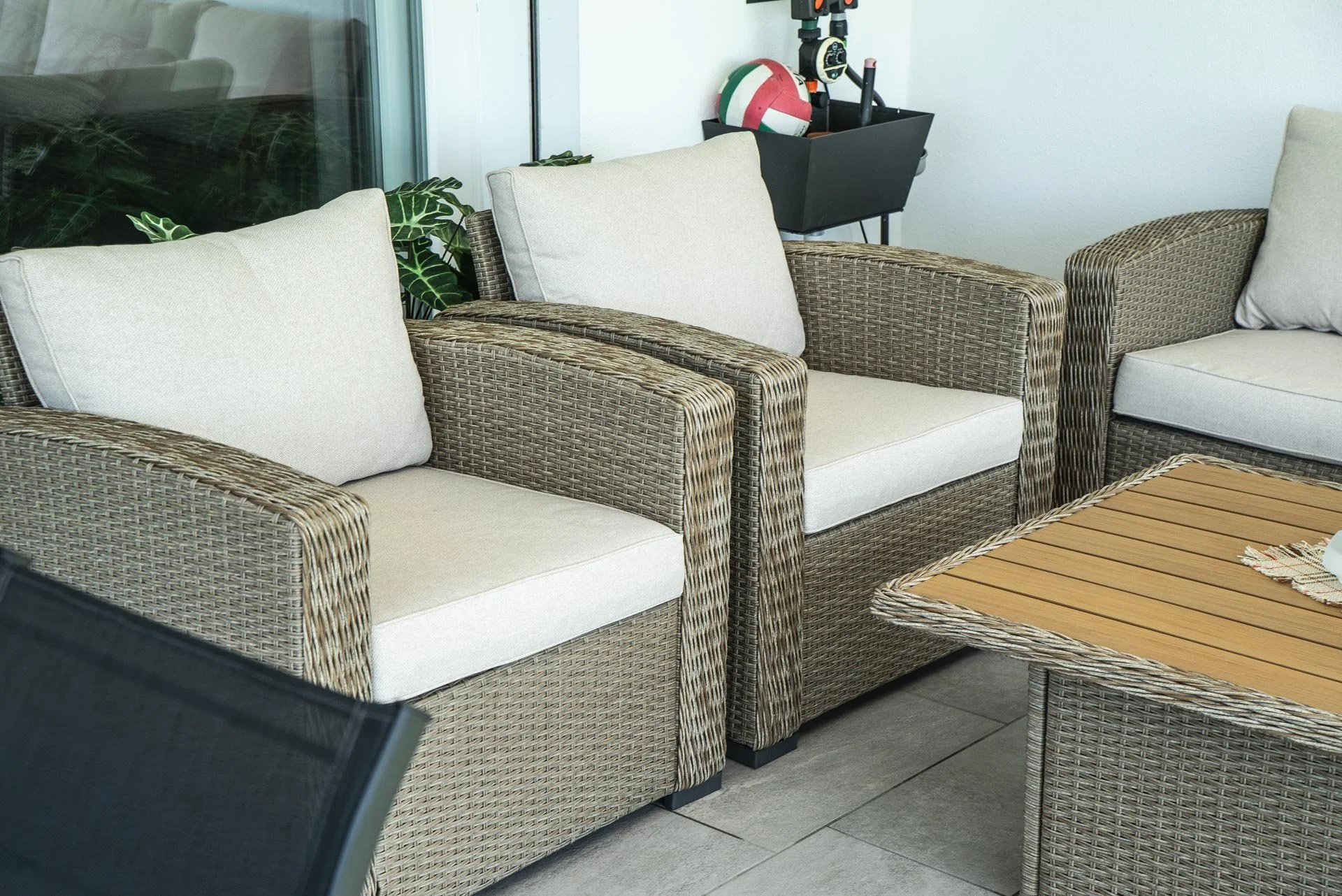 Soggiorno con divani in vimini, cuscini beige, tavolino in legno e piante verdi.