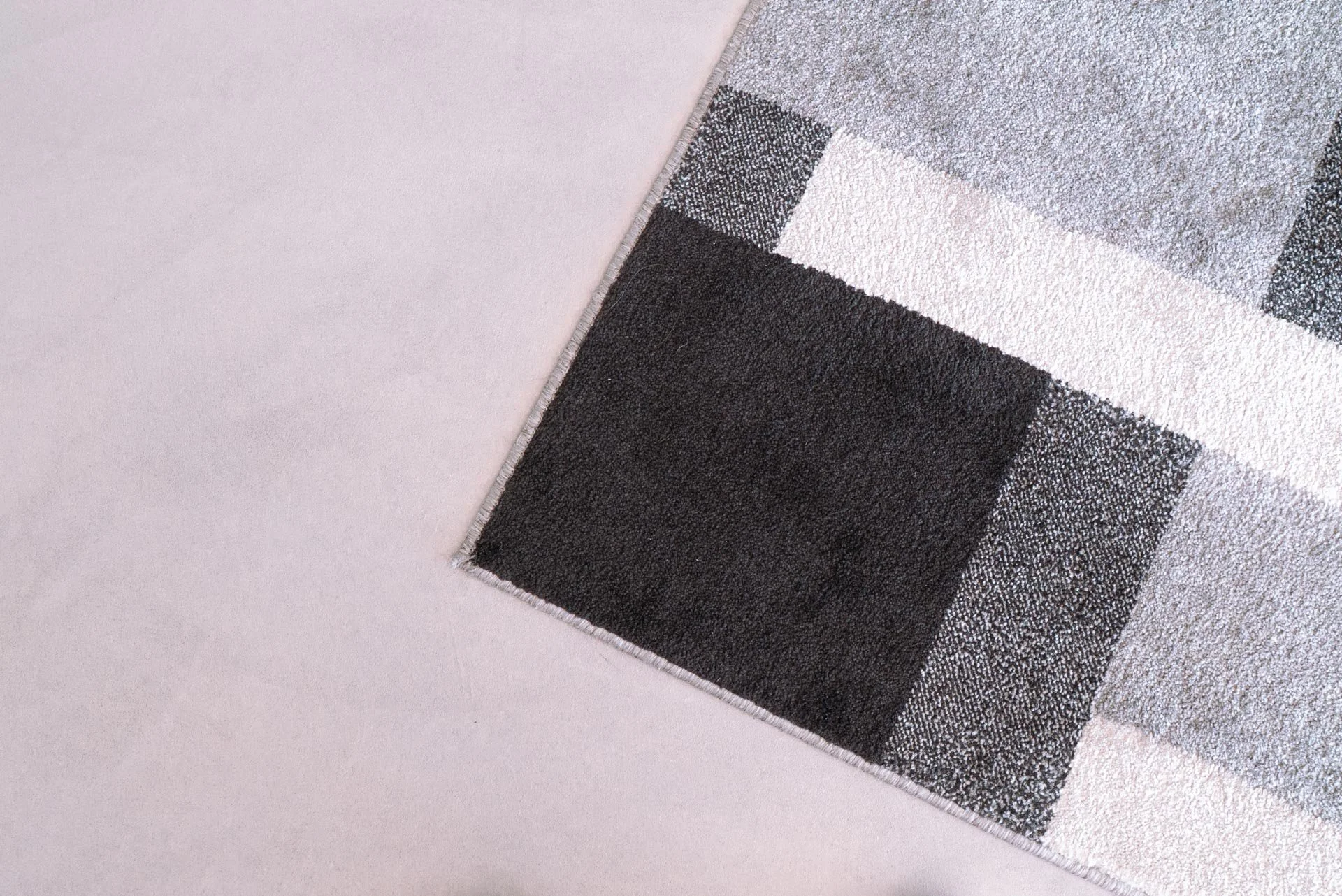 Tappeto con disegni geometrici nelle tonalità di grigio, bianco e nero, posizionato su un pavimento rosa chiaro.