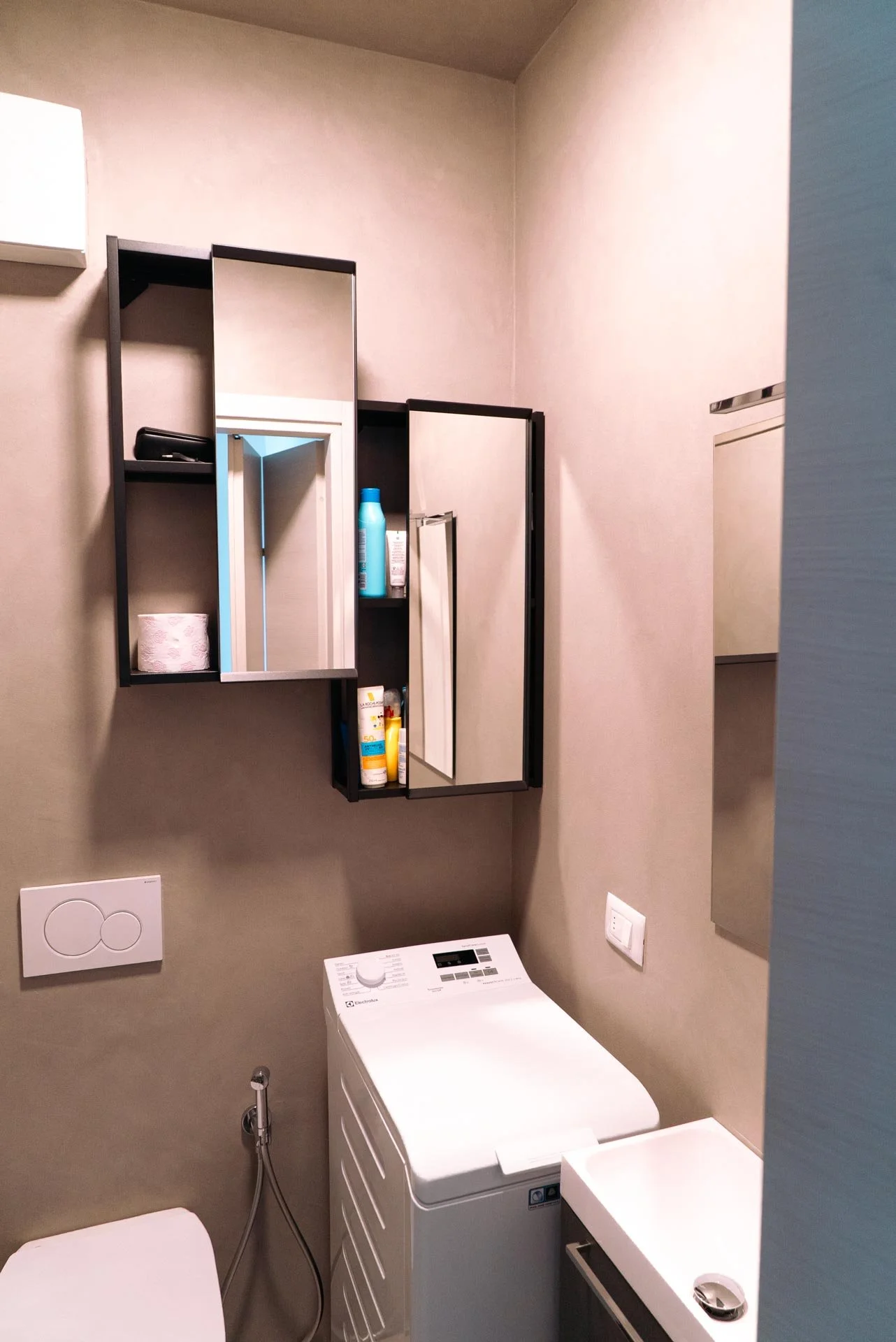 Lavatrice bianca in un bagno con specchietto e scaffali neri