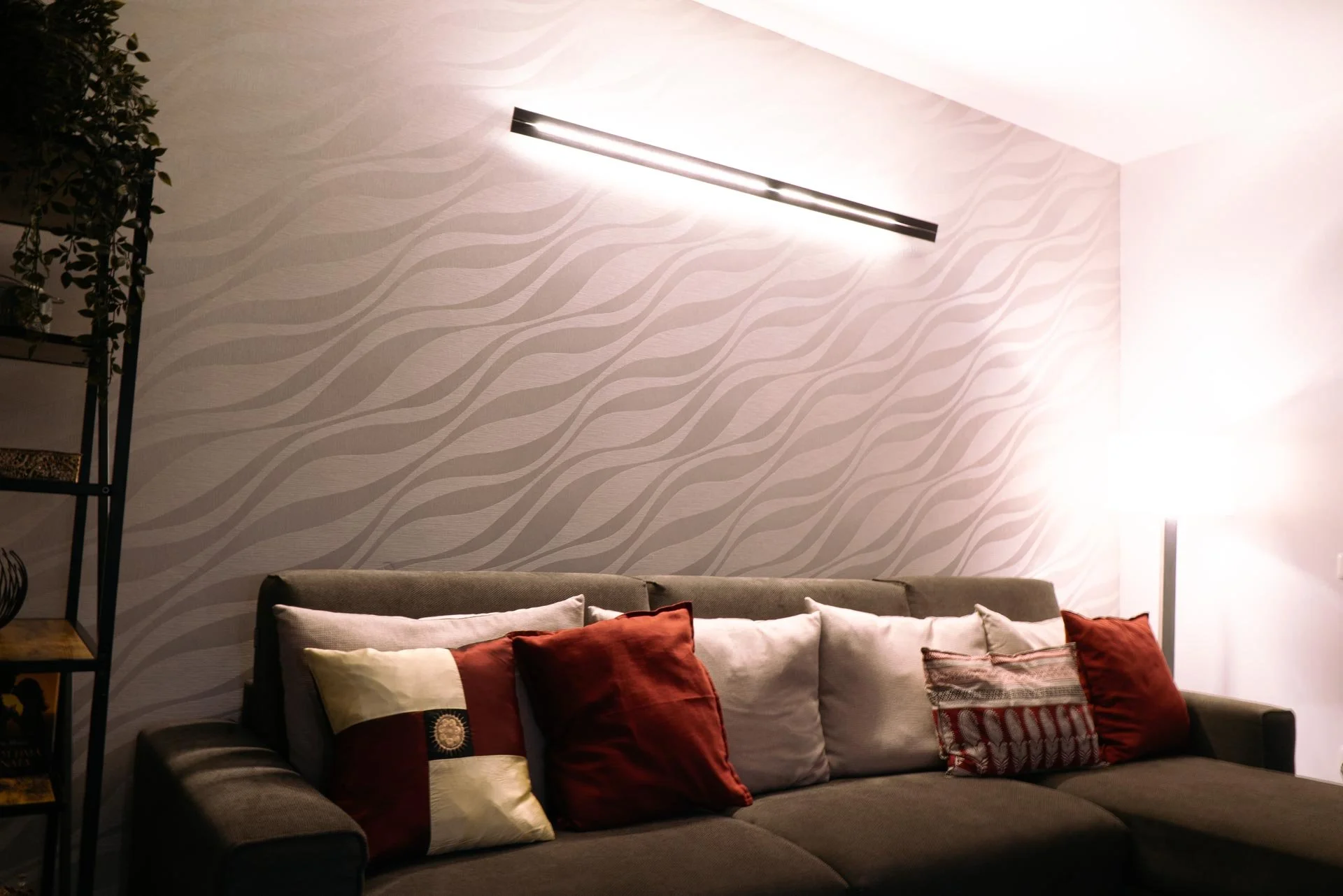 Soggiorno con divano marrone e cuscini di vari colori, parete con motivo ondulato e lampada a terra acceso
