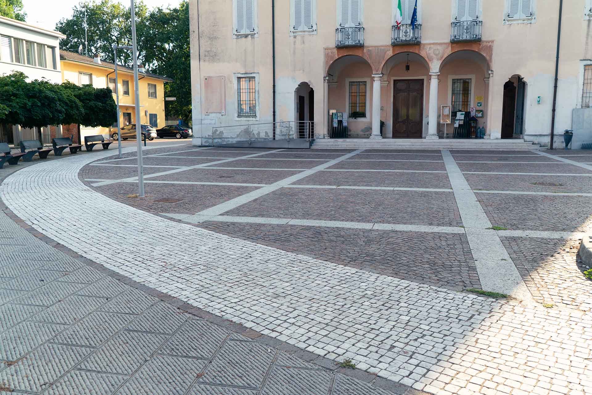 Piazza con pavimentazione in pietra, edificio storico con colonne e bandiere all'ingresso