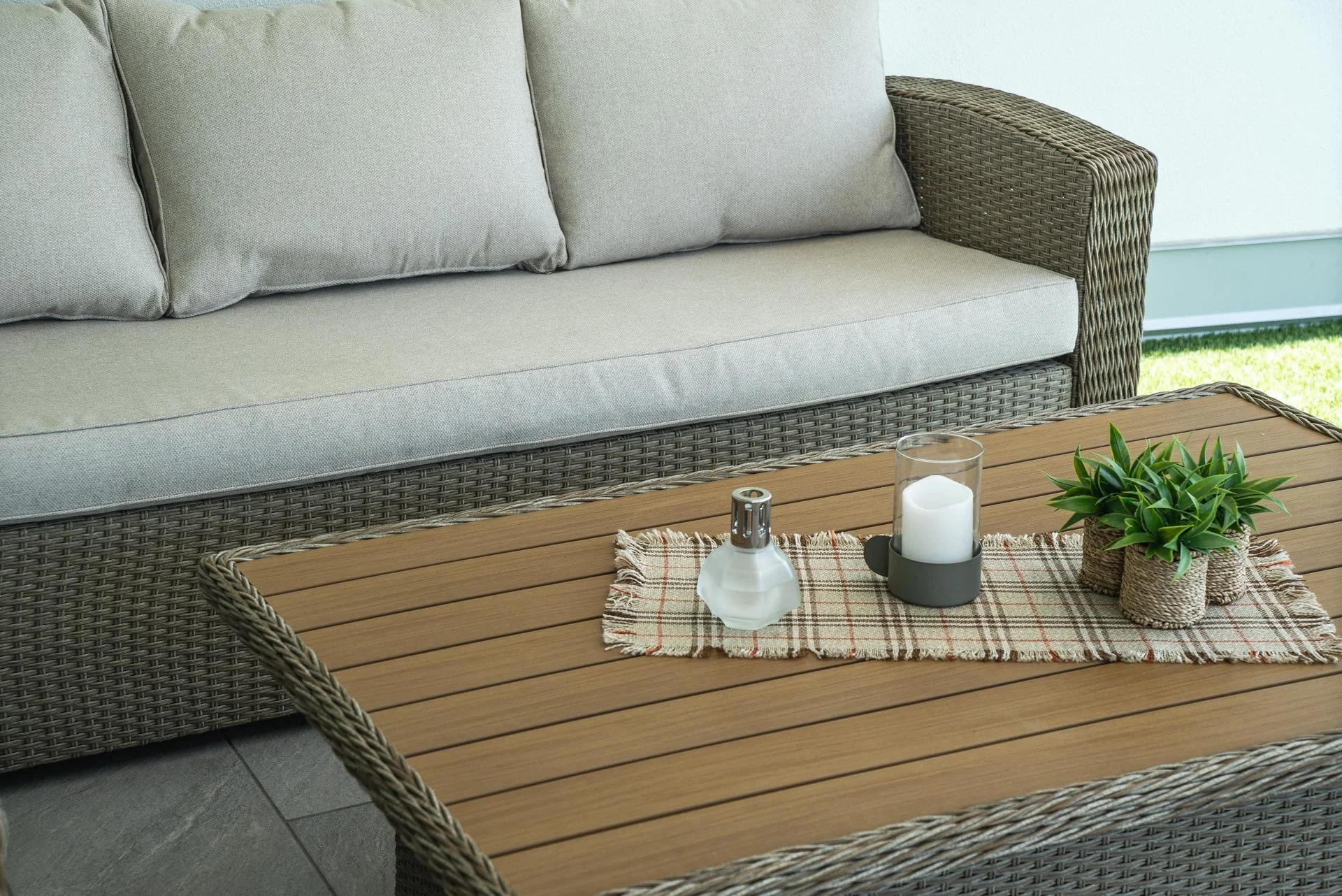 Soggiorno con divano in vimini, tavolo di legno con decorazioni di piante, candela e diffusore.