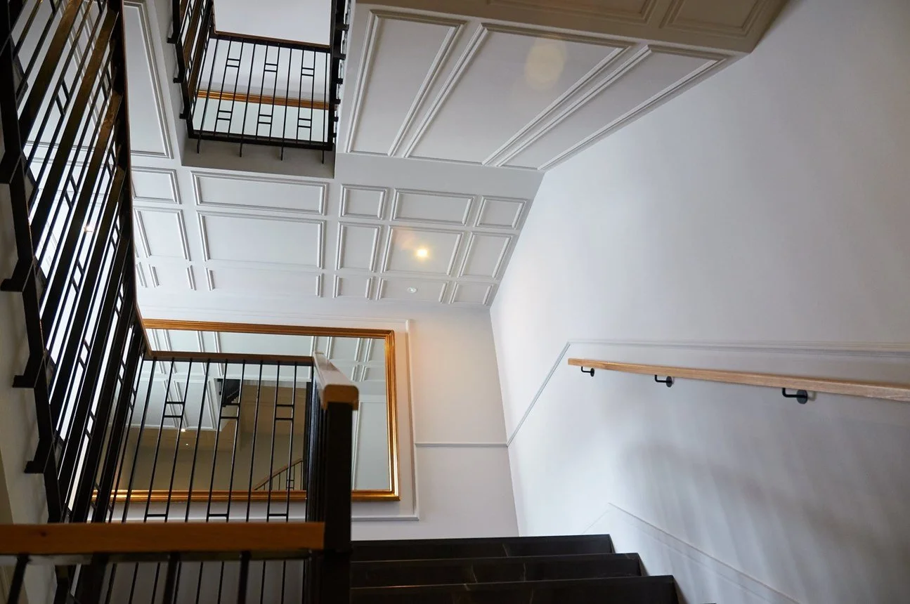 Scalinata interna con ringhiera metallica nera e pareti bianche con pannelli decorativi