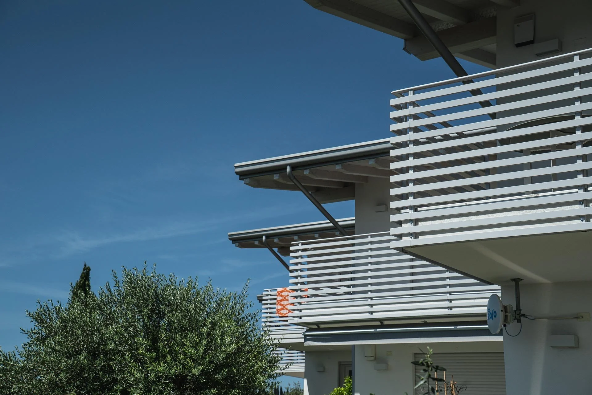 Edificio residenziale moderno con balconi e pannelli di ardesia bianca, sotto un cielo sereno.