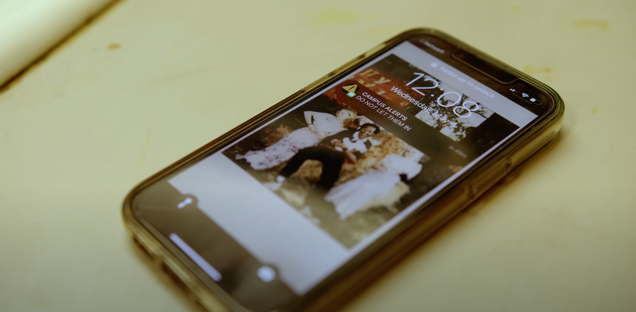 A smartphone lying on a light-colored surface, displaying a photo of two women sitting outdoors surrounded by autumn foliage.