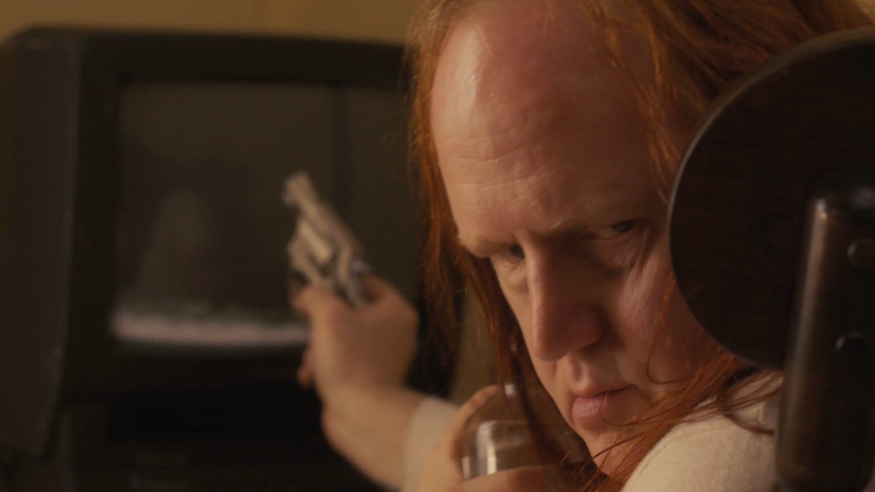 A person with long red hair pointing a gun at a vending machine.