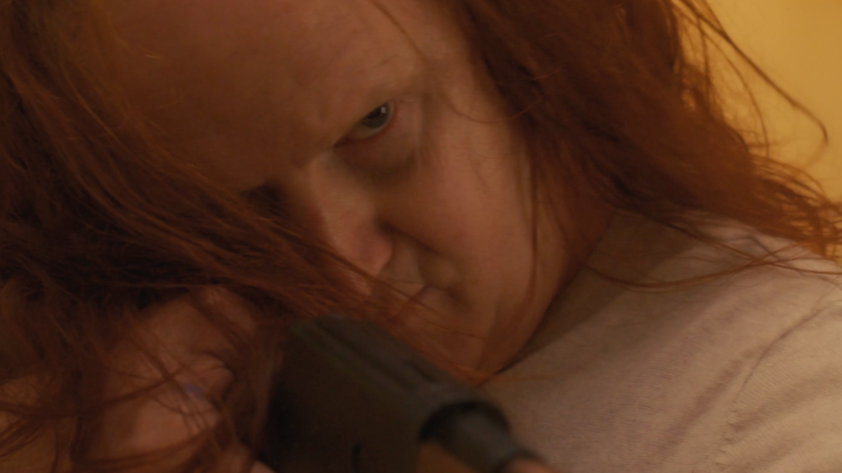 Close-up of a person with long, wavy red hair looking intently through a telescope.