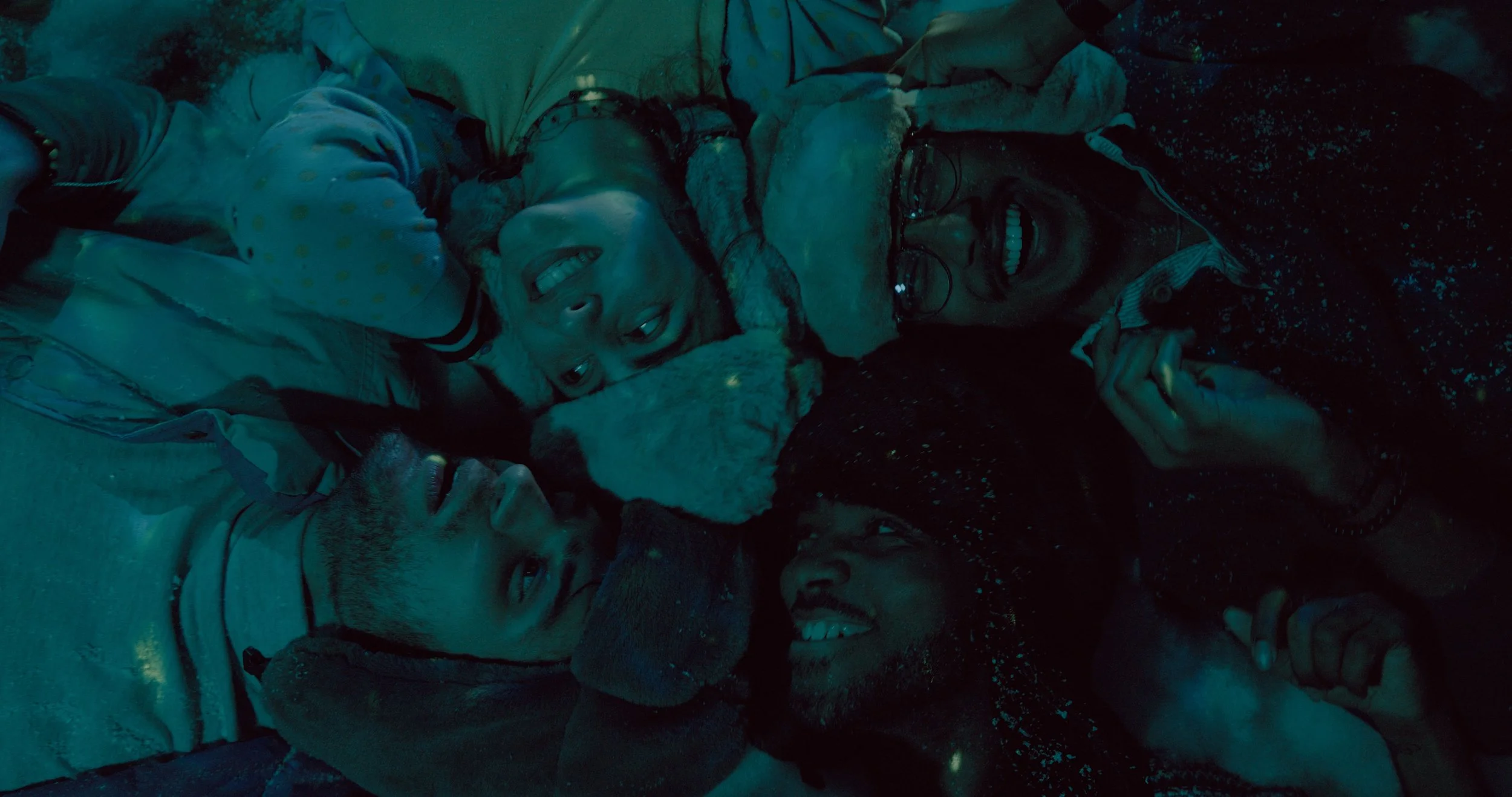 A group of five friends lying down close together, smiling, with a dog. The photo is taken at night.