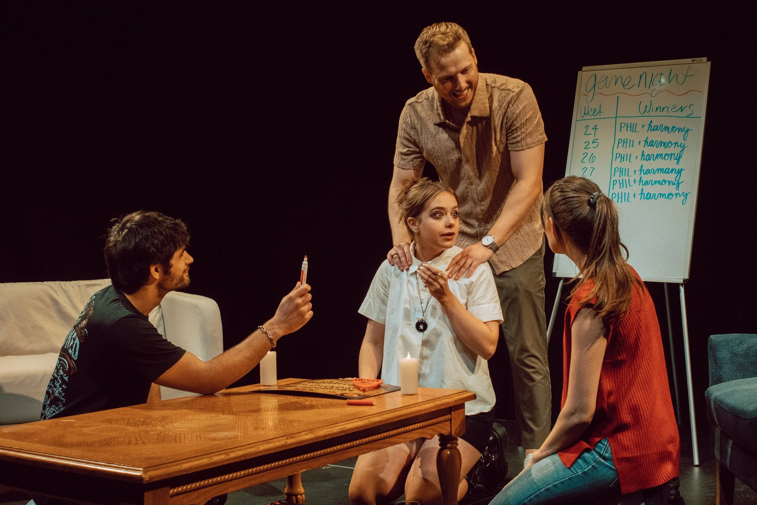 Group of five people engaged in a game or activity around a wooden table, with a whiteboard in the background displaying scores for game night.