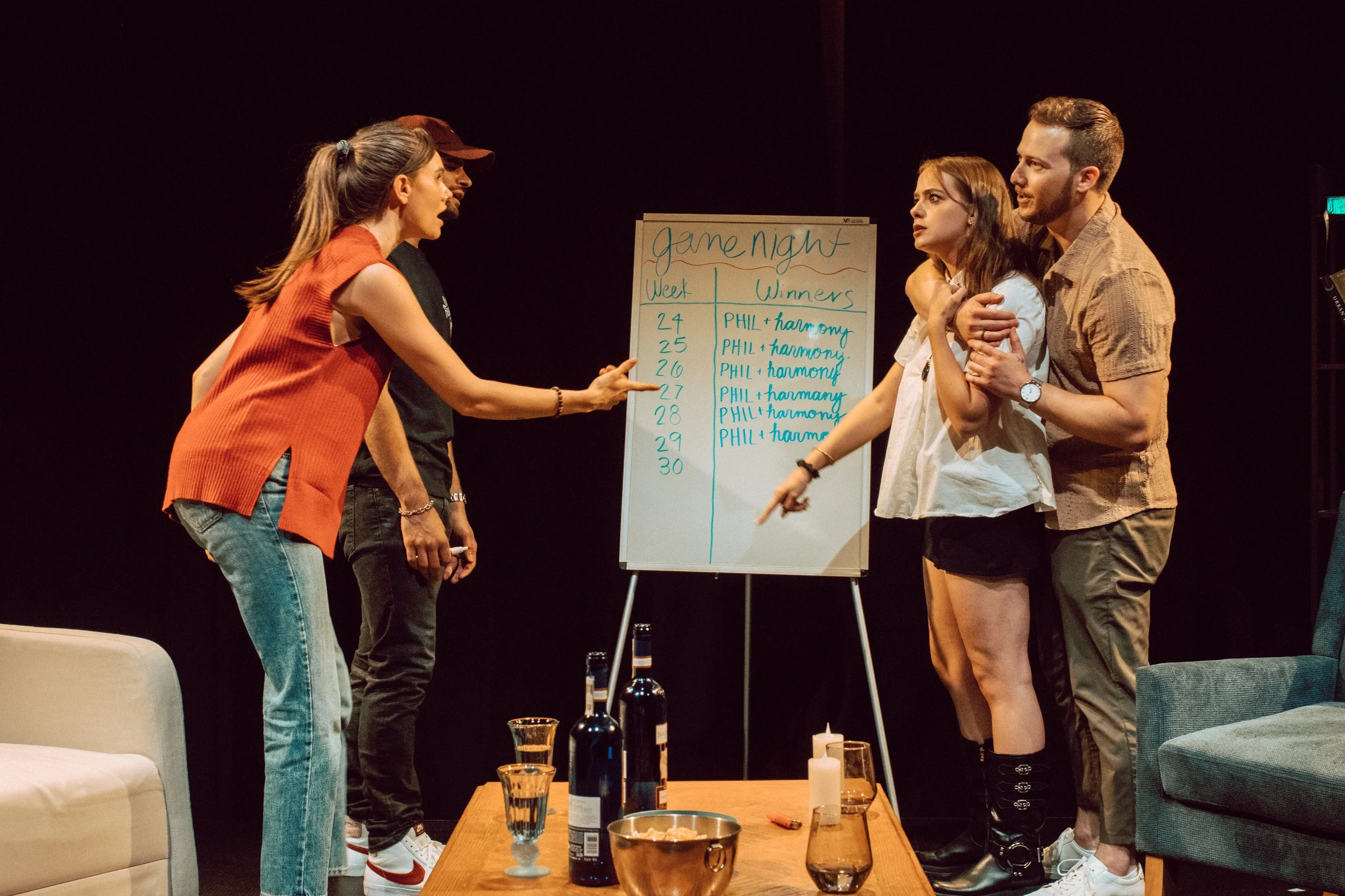 A group of six people standing around a whiteboard with a game night schedule on it, arguing or having a heated discussion.