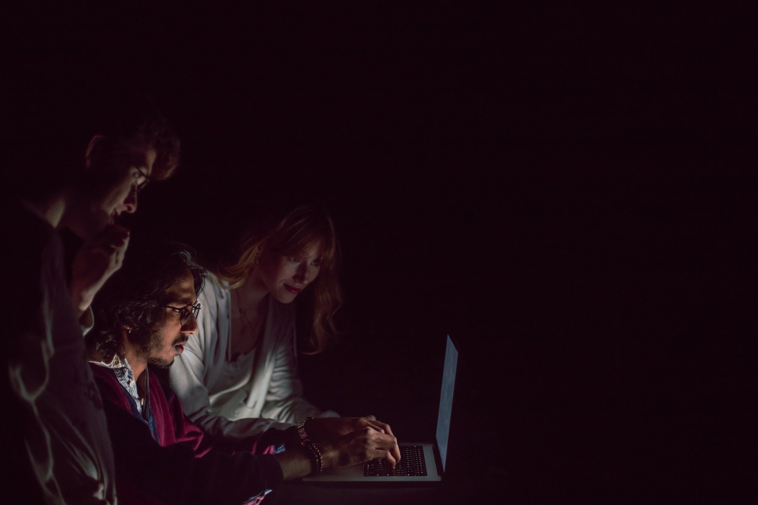Group of five people working together on laptops in a dark environment, focused on their screens.