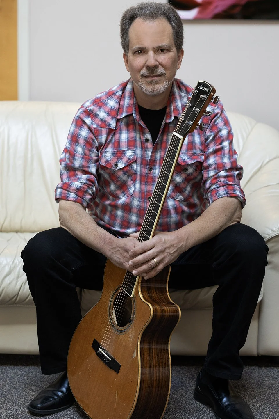 Dave Isaacs seated holding an acoustic guitar. Photo by Deone Jahnke.
