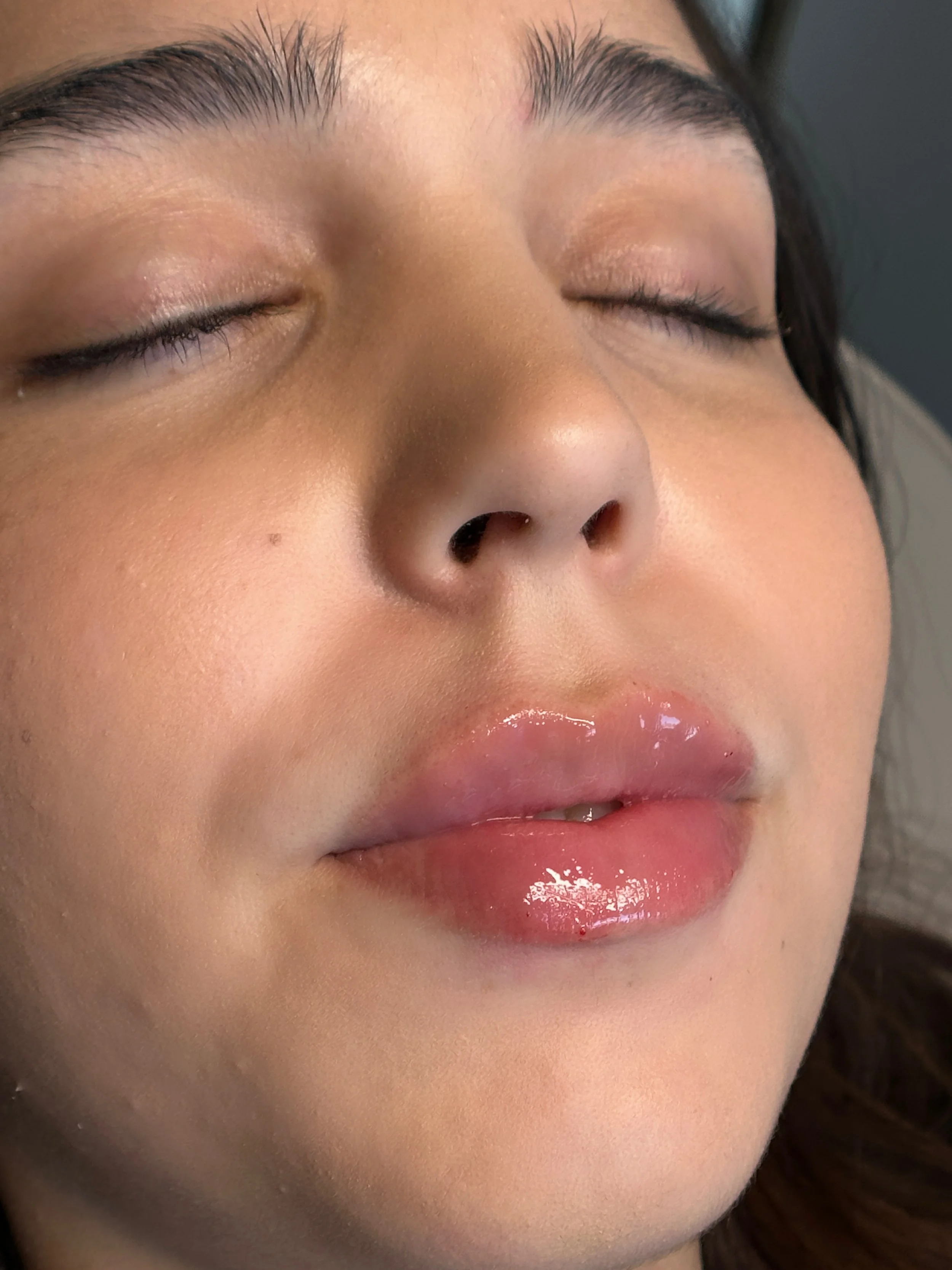 Close-up of a woman's face with closed eyes, glossy lips, and smooth skin.