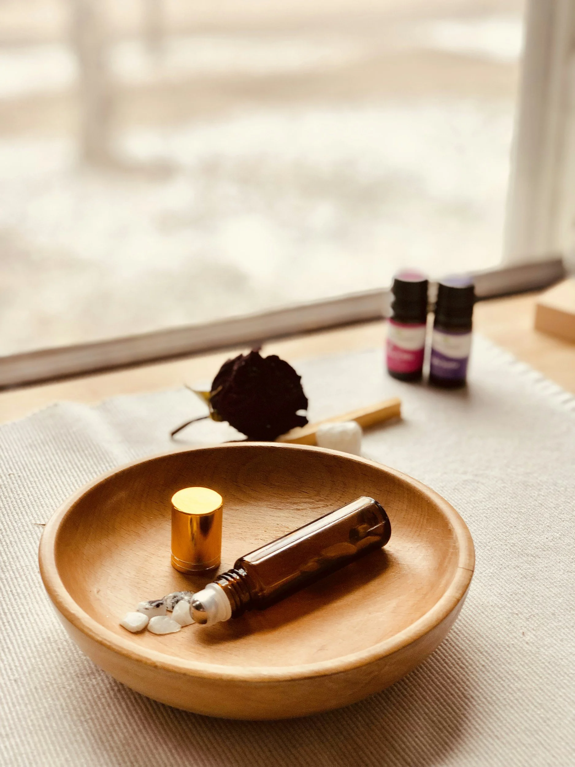 Essential oils and herbs on a wooden dish near a window