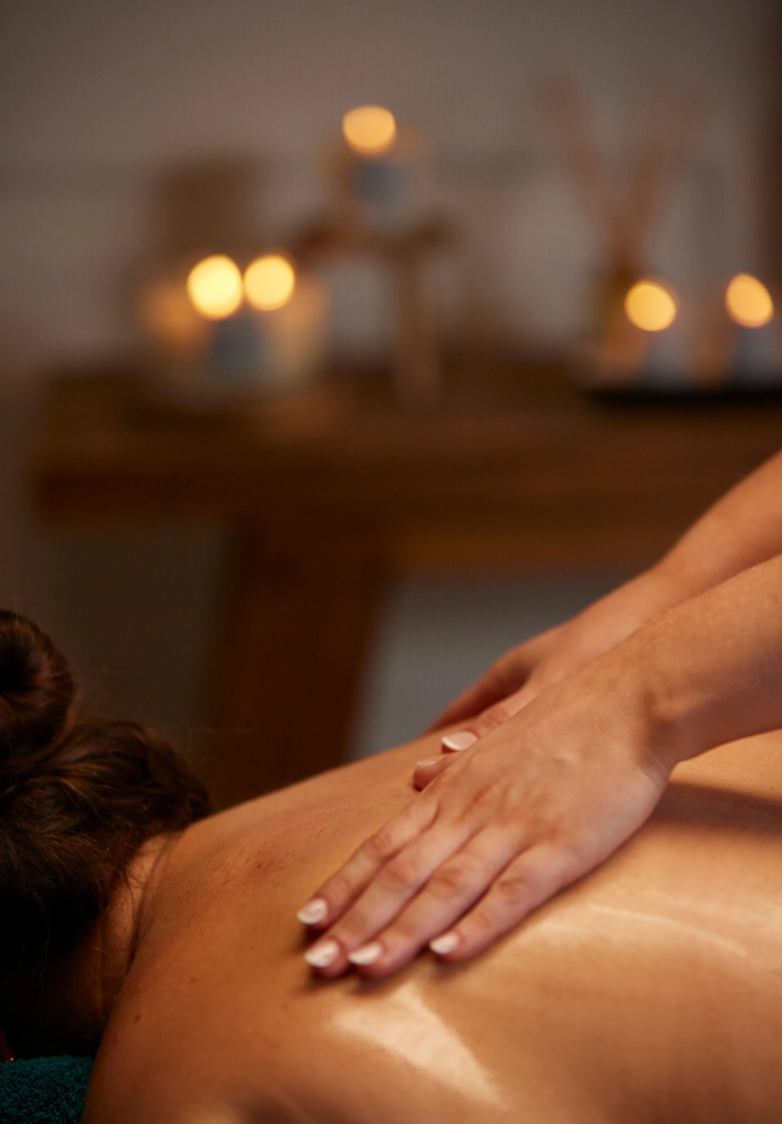 Close-up of a woman receiving a massage, with candles blurred in the background for a relaxing atmosphere.