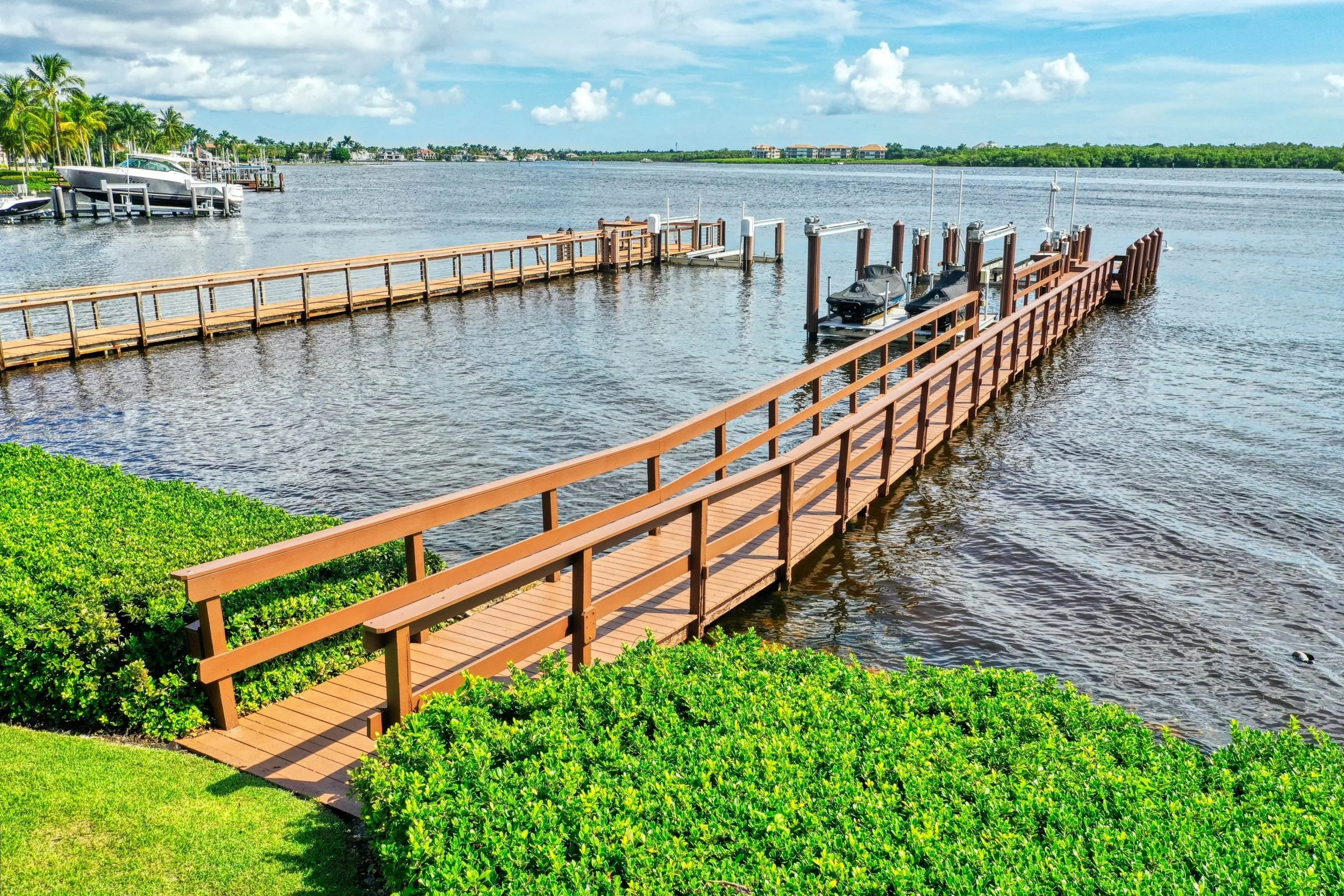 Dock extending into water with boats and green hillside, cloudy sky