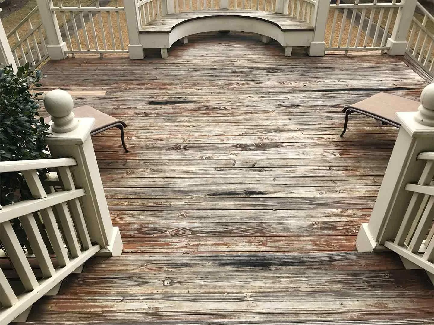 A wooden porch with two benches, white railings, and a curved set of stairs leading down.