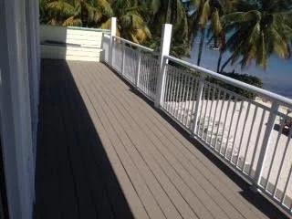 View of a wooden deck with a white railing overlooking palm trees and the ocean