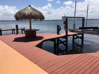 A lakeside dock with a thatched umbrella, benches, and a wooden pier extending over calm water during daytime.