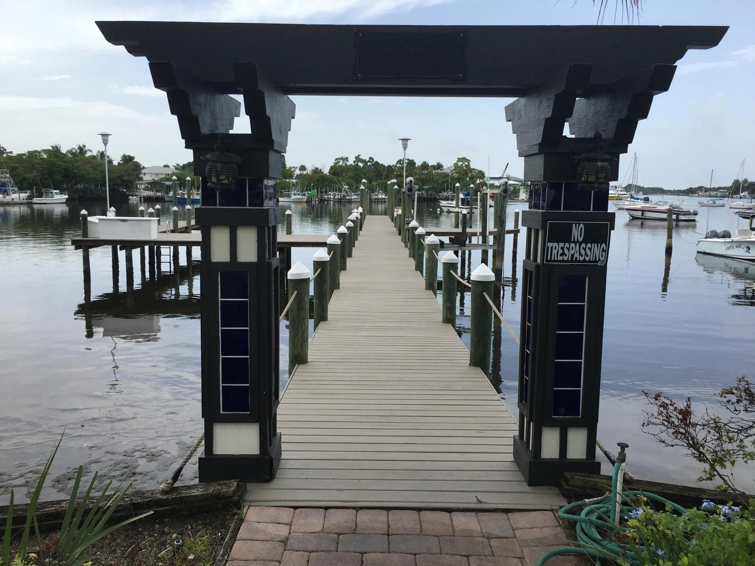 Dock extending over calm water with boats and sailboats, entrance with archway, and a sign that says 'No Trespassing.'