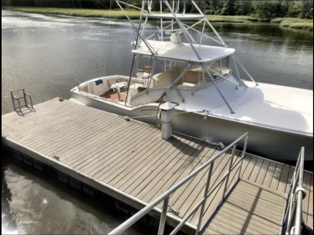 A white boat docked at a wooden pier on a river with trees in the background.