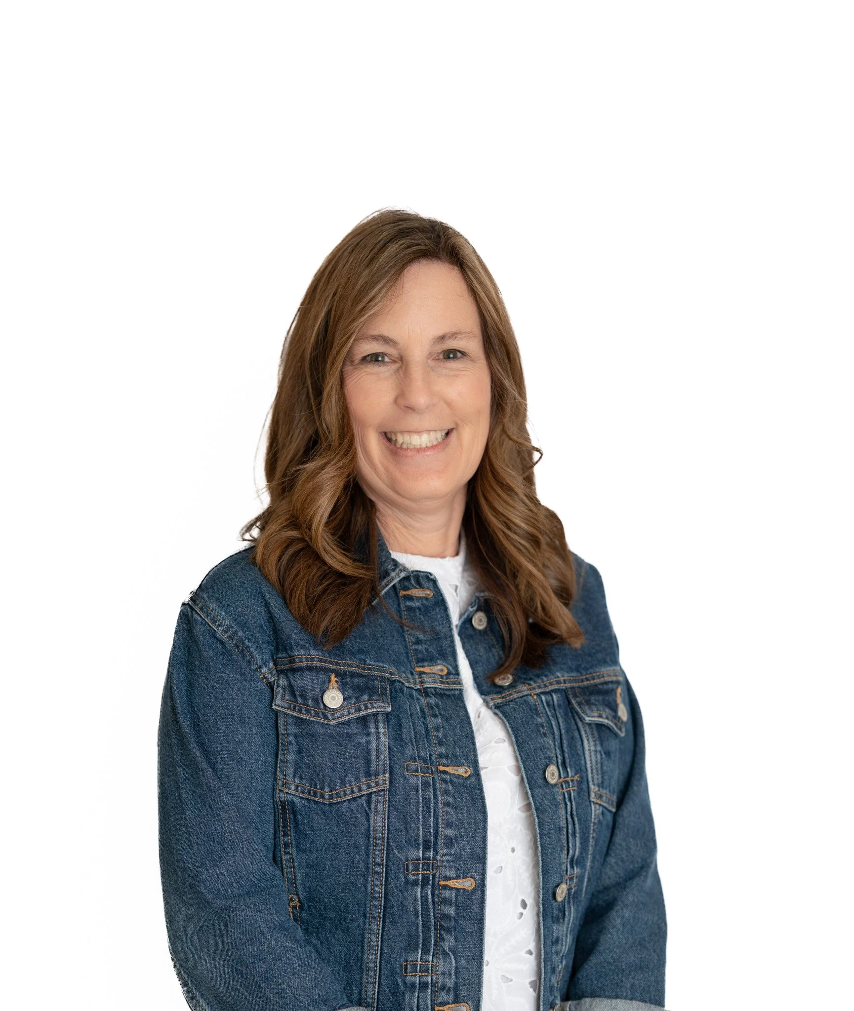 A woman with shoulder-length brown hair smiling, wearing a denim jacket over a white shirt, against a plain white background.