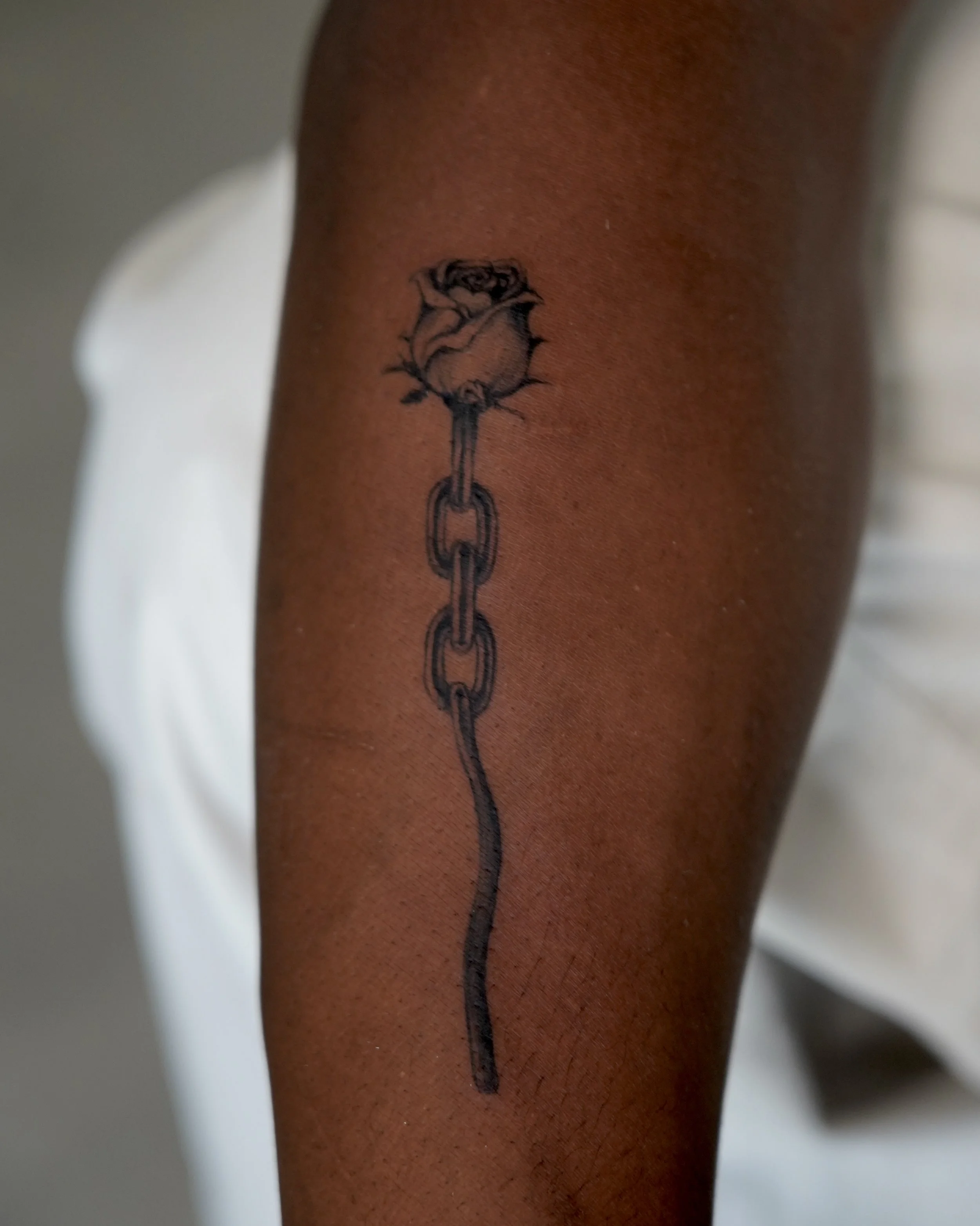 Tattoo of a rose with thorns, connected to a broken chain, on a person's arm.