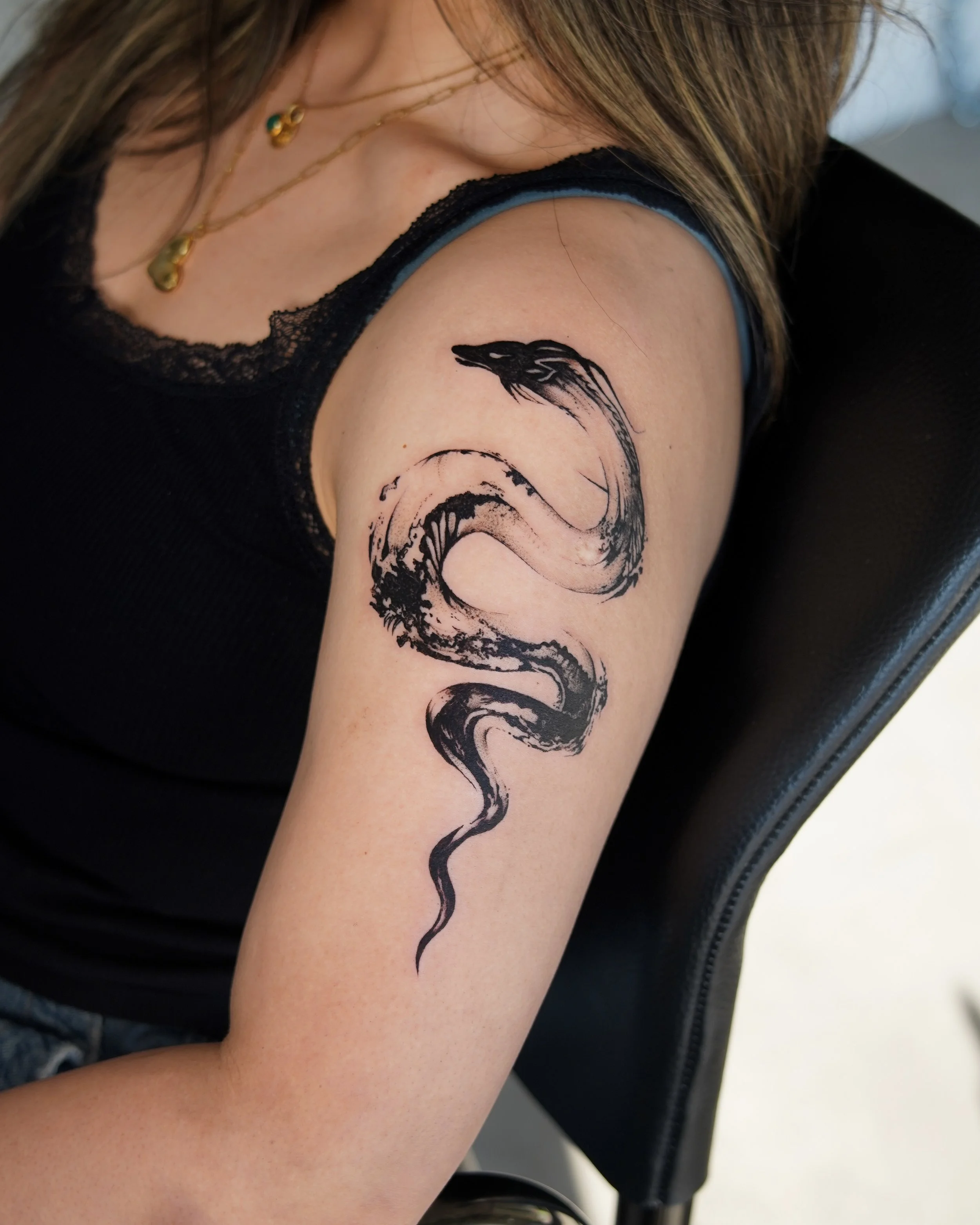 Tattoo of a black, stylized snake on a person's upper arm.