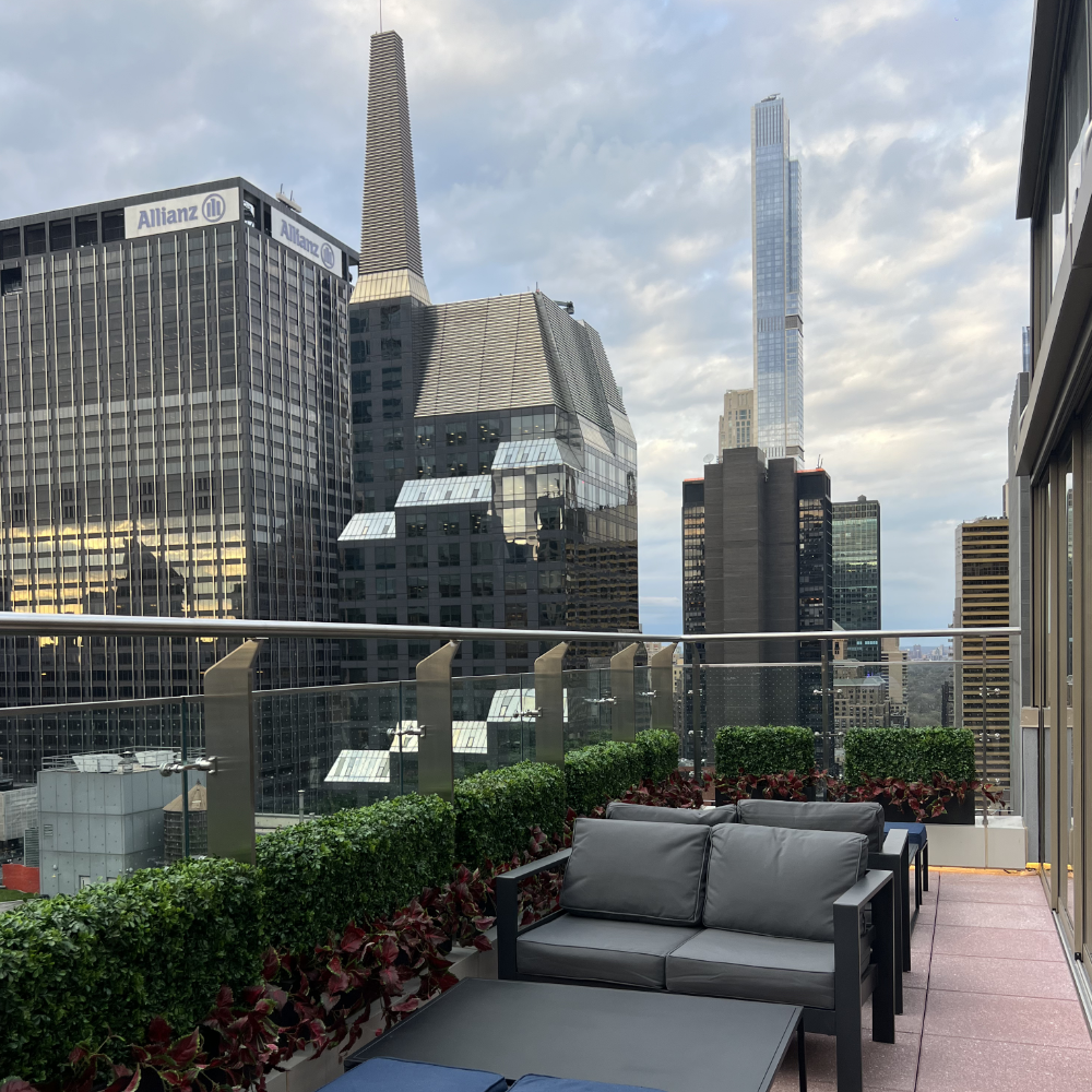 City skyline view from a balcony with modern black furniture, green plants, and skyscrapers, including the Willis Tower and the Salesforce Tower, under a cloudy sky.
