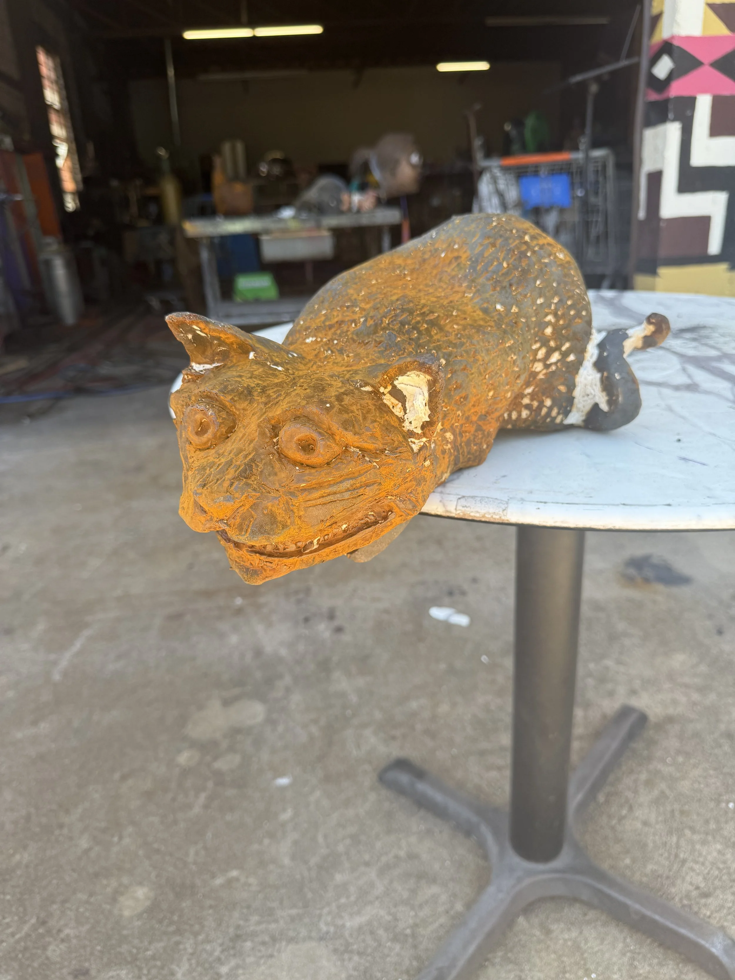 cast iron sculpture of a cat with large eyes and toothy grin