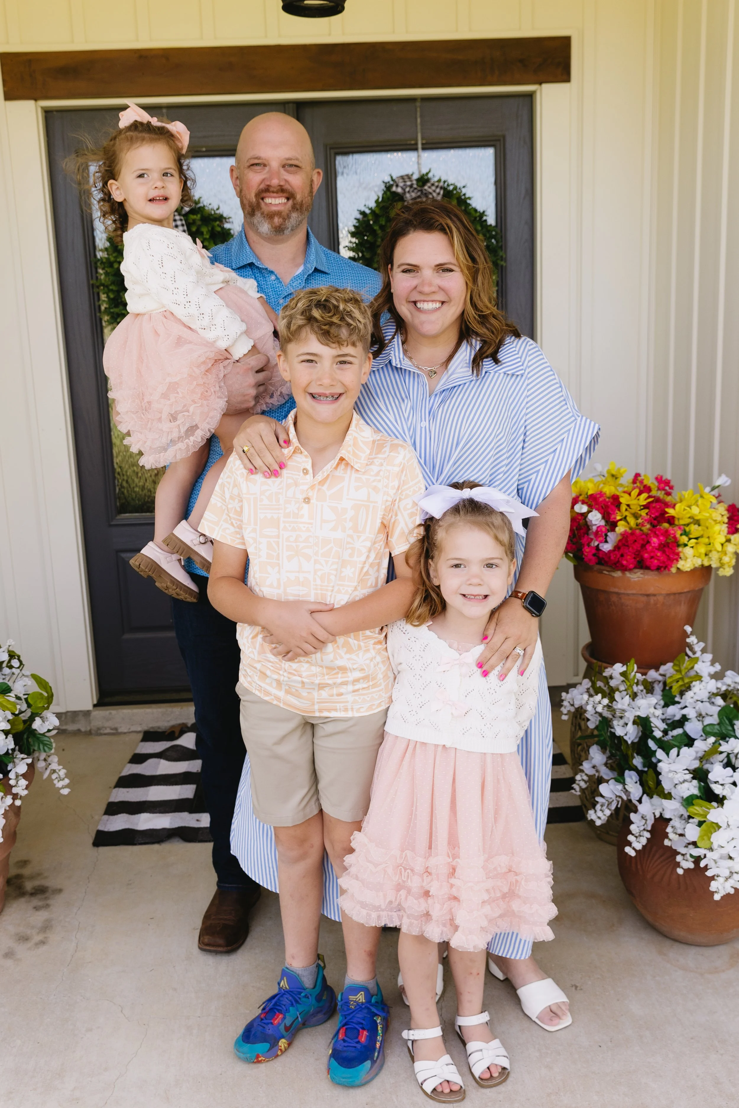 A group of five people, including two adults and three children, standing in front of a door decorated with wreaths, posing for a photo and smiling.
