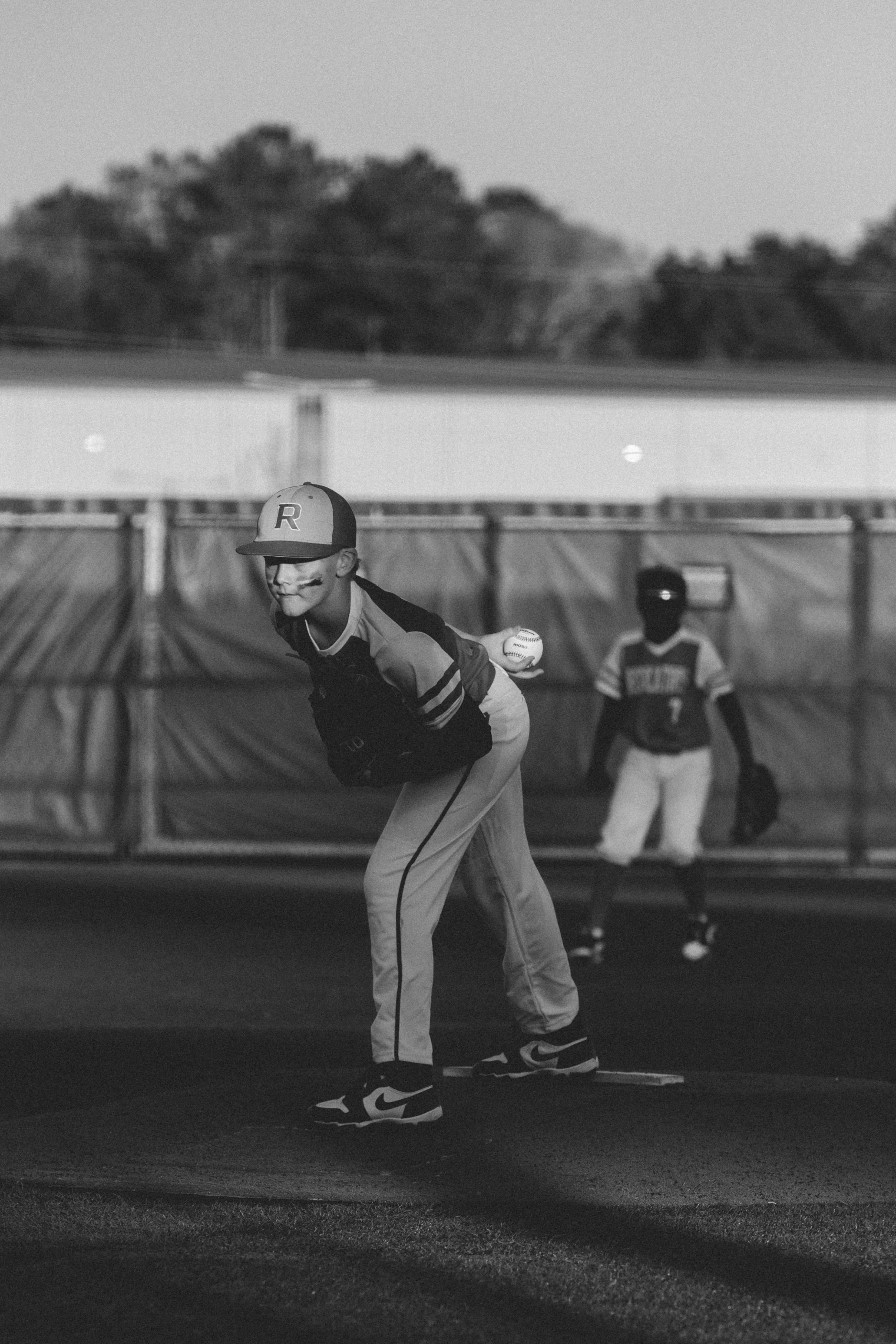 A baseball player with a batting helmet and uniform is preparing to bat on a baseball field, with another player standing in the background.