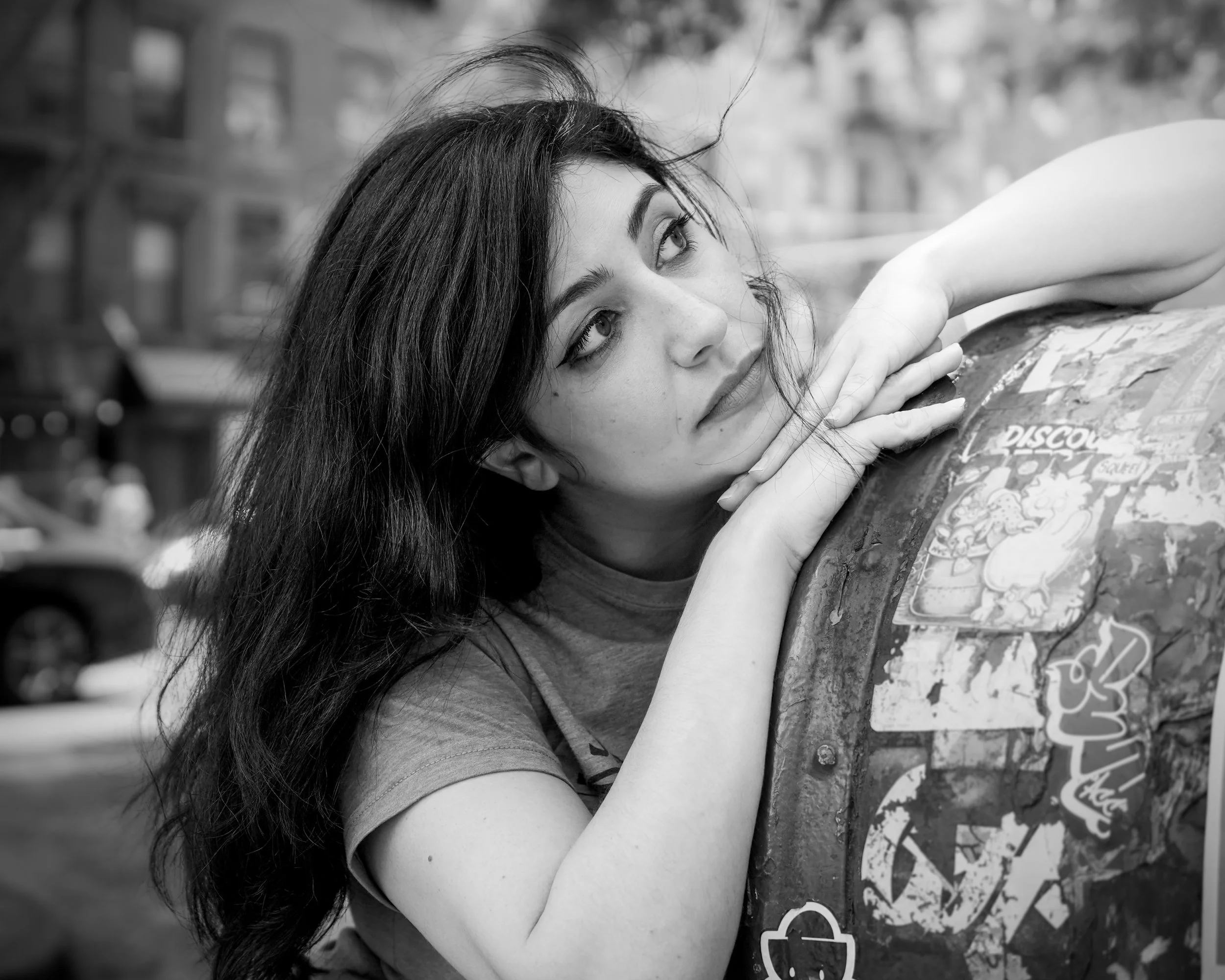 A young woman with long dark hair lying on her side on a graffiti-covered surface, resting her head on her hand, gazing upward.