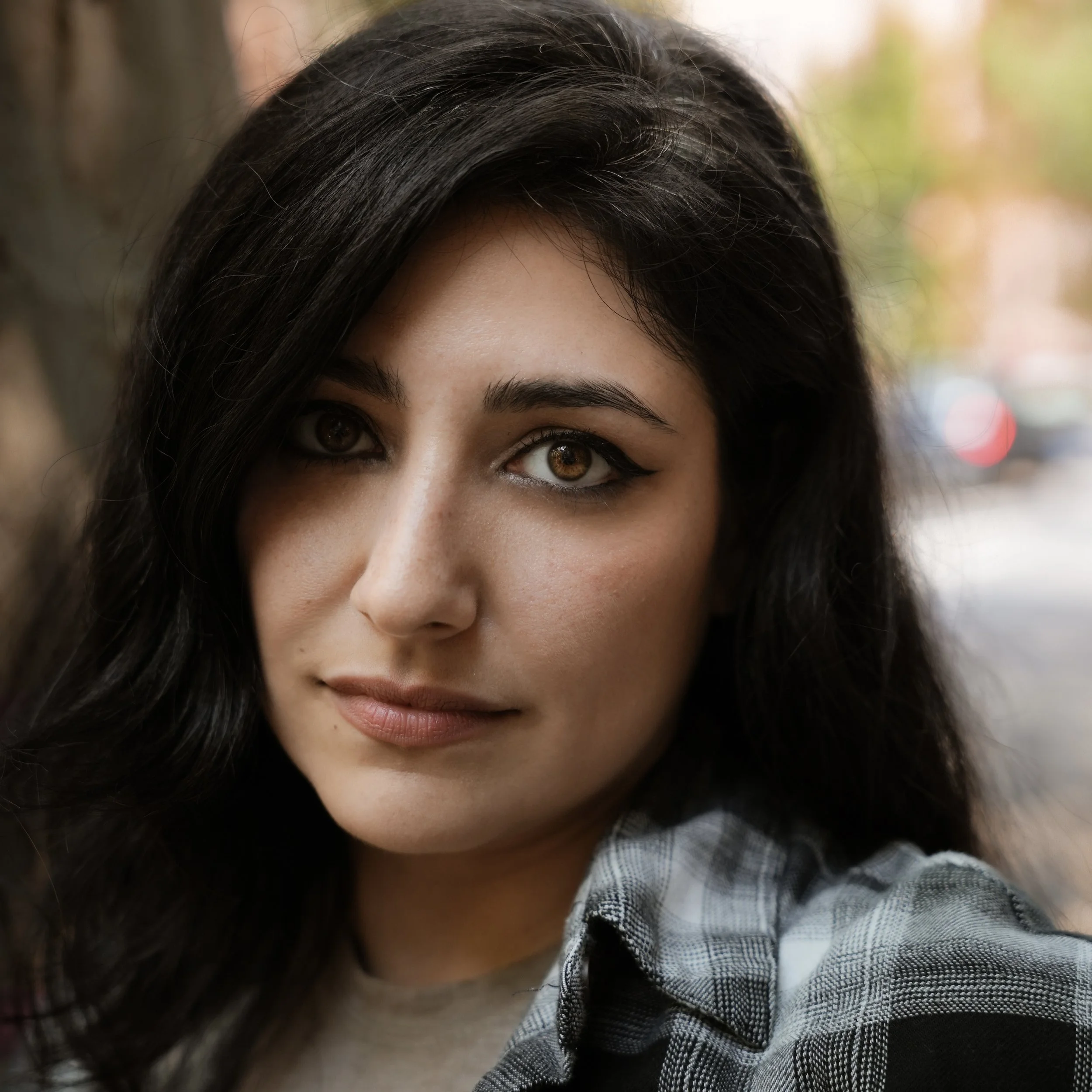 Close-up of a woman with dark brown hair and brown eyes, wearing a black and white plaid shirt.